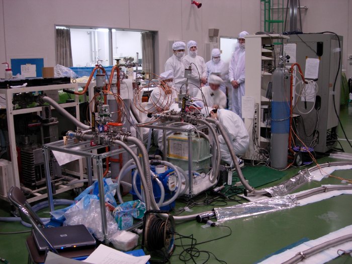 Six men in white cleanroom garb watch a large gas-flow meter. (94K JPEG)