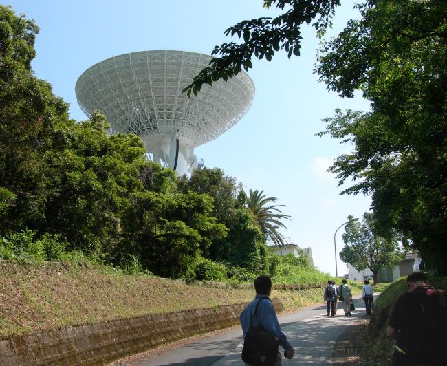 Several team members in relatively light clothing stroll up the shaded path to a large radio antenna. (88K JPEG)