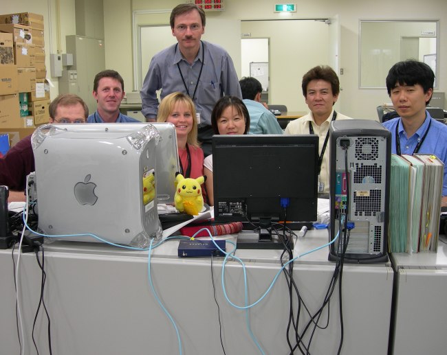 Team members as described in the caption are partially visible over the tops of their computer monitors. (71K JPEG)