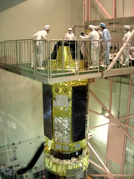 Seven people in clean-room suits look on as they take photos of the top of the satellite, which protrudes through the platform on which they stand. (68K JPEG)