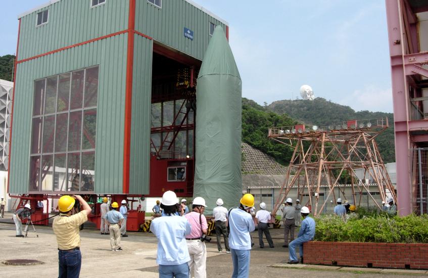 Under a perfect blue sky, the satellite atop the third stage, wrapped in light gray blanketing, towers 25 feet over the crowd watching intently as it is slowly rolled toward the launch tower just in frame on the right. (82K JPEG)