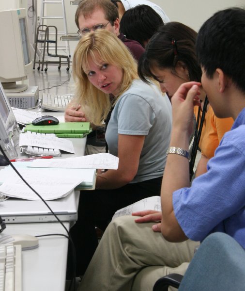 Intense looks wash across the faces of several people in front of their computers.  Intense and sleepy. (57K JPEG)