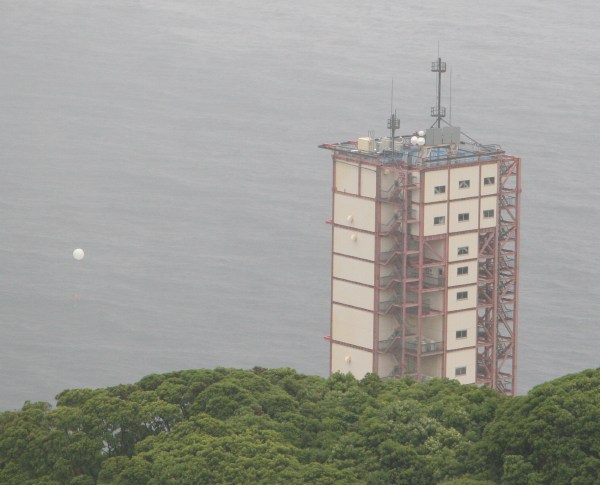 A greyness permeates the image of the launch tower, as the small globe of a weather balloon appears to its left. (53K JPEG)