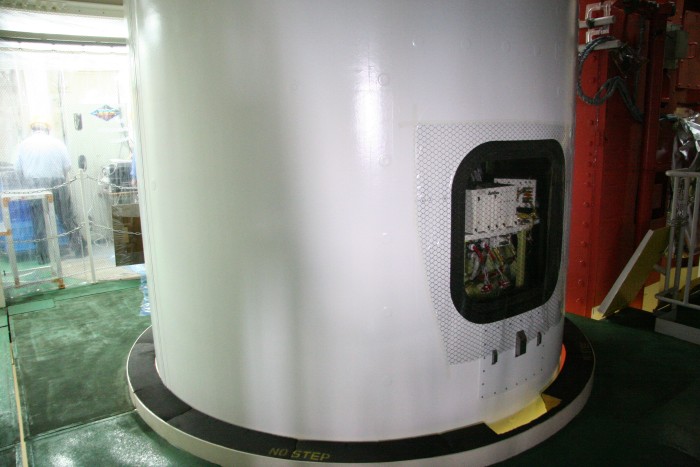 The pure white cylinder of the rocket projects through the floor and out of frame above, while a 50 x 50 centimeter square hole is covered with a layer of plastic. (65K JPEG)