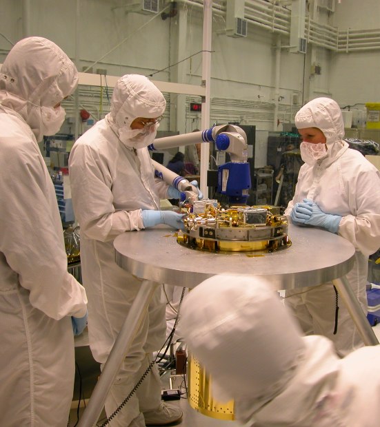 The helium insert protrudes through the top of the aluminum stand, as well as hanging below.  On the top, one engineer uses a futuristic-looking multi-jointed arm to measure it as the lead engineer looks on happily. (76K JPEG)