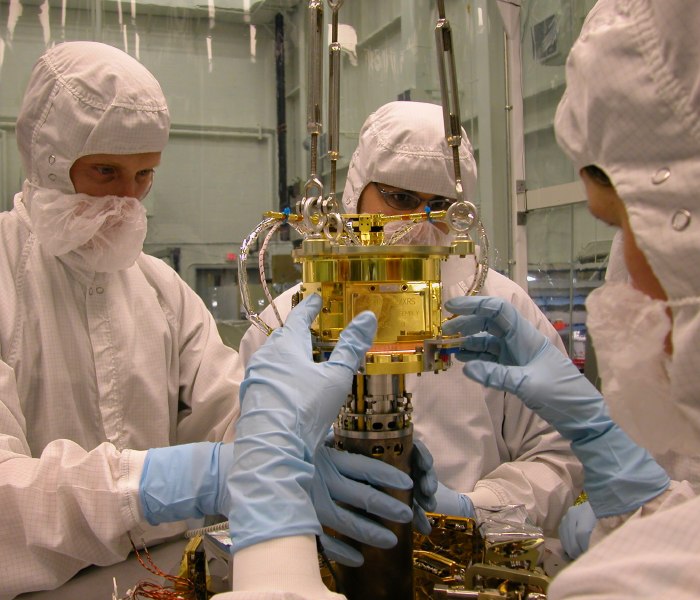 Gloved hands gently guide the 7 cm diameter ADR cylinder into a hole, out of frame at the bottom.  (92K JPEG)